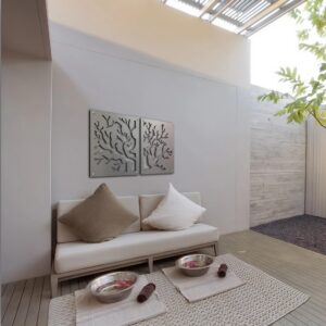 Modern seating area with decorative coral wall art, bowls, and a small tree in a serene space.