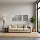 A cozy living room features a light sofa, three abstract wall art pieces, a floor lamp, and a potted plant.
