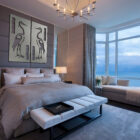 Stylish bedroom featuring a large bed, artwork of herons, and a view of the ocean through large windows.