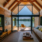 Modern interior with large windows, showcasing a view of a lake and outdoor seating area.