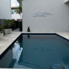 A swimming pool reflects the sky, with decorative wave art on the wall and potted plants nearby.