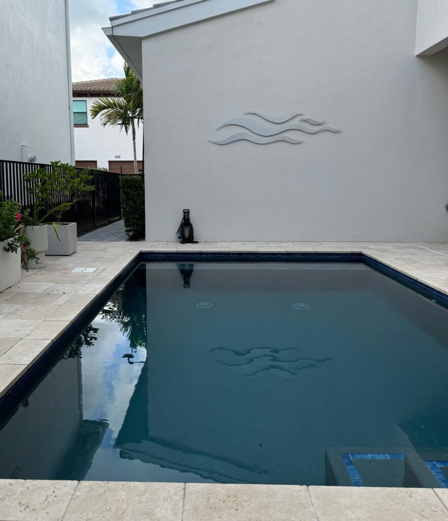 A swimming pool reflects the sky, with decorative wave art on the wall and potted plants nearby.