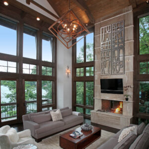 Spacious living room with large windows, modern chandelier, and a fireplace. Cozy furniture and decorative accents present.