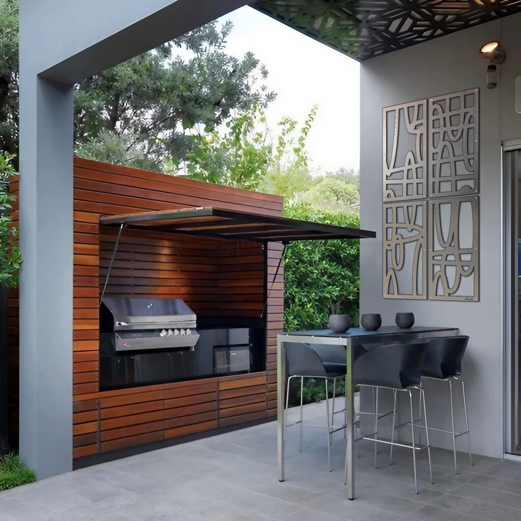 Outdoor kitchen features a grill, modern seating, and decorative wall art surrounded by greenery.