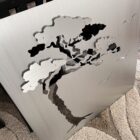 Metal panel features a cutout design of a tree and birds, resting on a textured carpet.