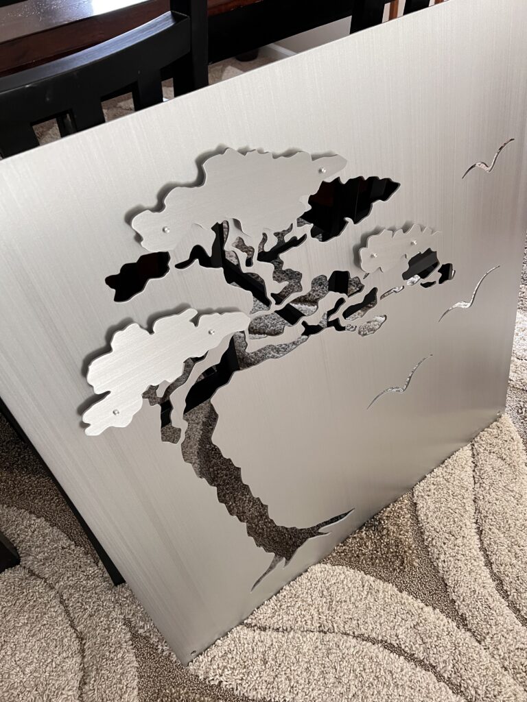 Metal panel features a cutout design of a tree and birds, resting on a textured carpet.