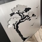Metal art piece featuring a tree silhouette and birds against a brushed silver background.