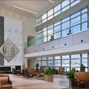 Modern lobby with large windows, decorative wall, seating areas, and indoor plants.