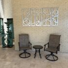 Two rocking chairs and a small table sit against a textured wall, with abstract metal art above. A sculpture is nearby.