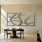 A modern wall art piece with abstract patterns hangs above a round table and chairs in a bright office space.