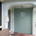 A small porch features a wicker chair, a light fixture, and a decorative wall piece on a mint green wall.