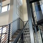 Modern staircase with black railings, leading to a wall art piece and large windows.