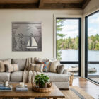 A cozy living room features a boat and palm tree wall art, with a view of a lake and trees outside.