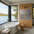 Modern bathroom features a freestanding tub, large windows, and artistic wall panels depicting abstract figures.