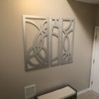 Three abstract metal wall panels with curved designs hang above a bench in a neutral-toned hallway.