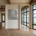 Two metal seahorse artworks hang on a white wall in a bright, modern room with large windows overlooking a lake.