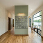 A hallway features a green wall with four abstract framed artworks, large windows showing a lakeside view.