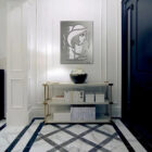 A modern hallway features a metal artwork, a vase with flowers, and a shelf with books.