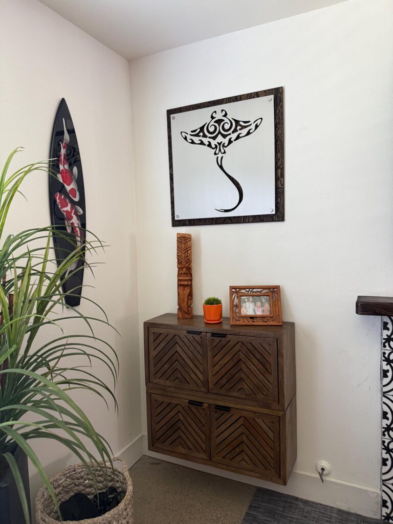 A corner with a wooden cabinet, decorative plant, framed photo, and manta ray artwork on the wall.