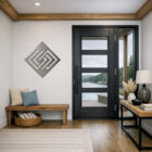 Modern foyer with a geometric wall art, wooden bench, and large glass door revealing a scenic view.