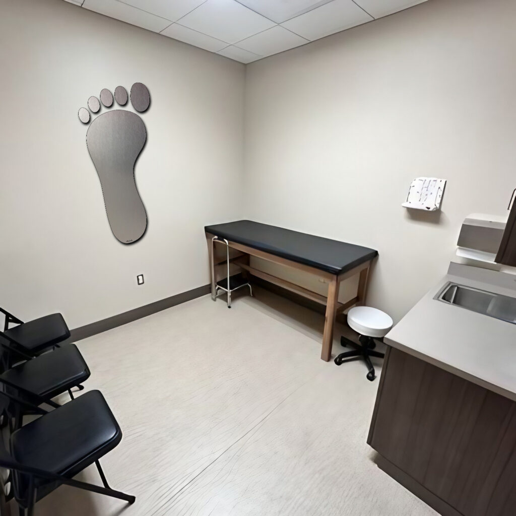 A medical examination room with a foot-shaped wall decoration, a treatment table, and several chairs.