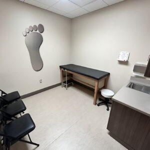 A medical examination room with a foot-shaped wall decoration, a treatment table, and several chairs.