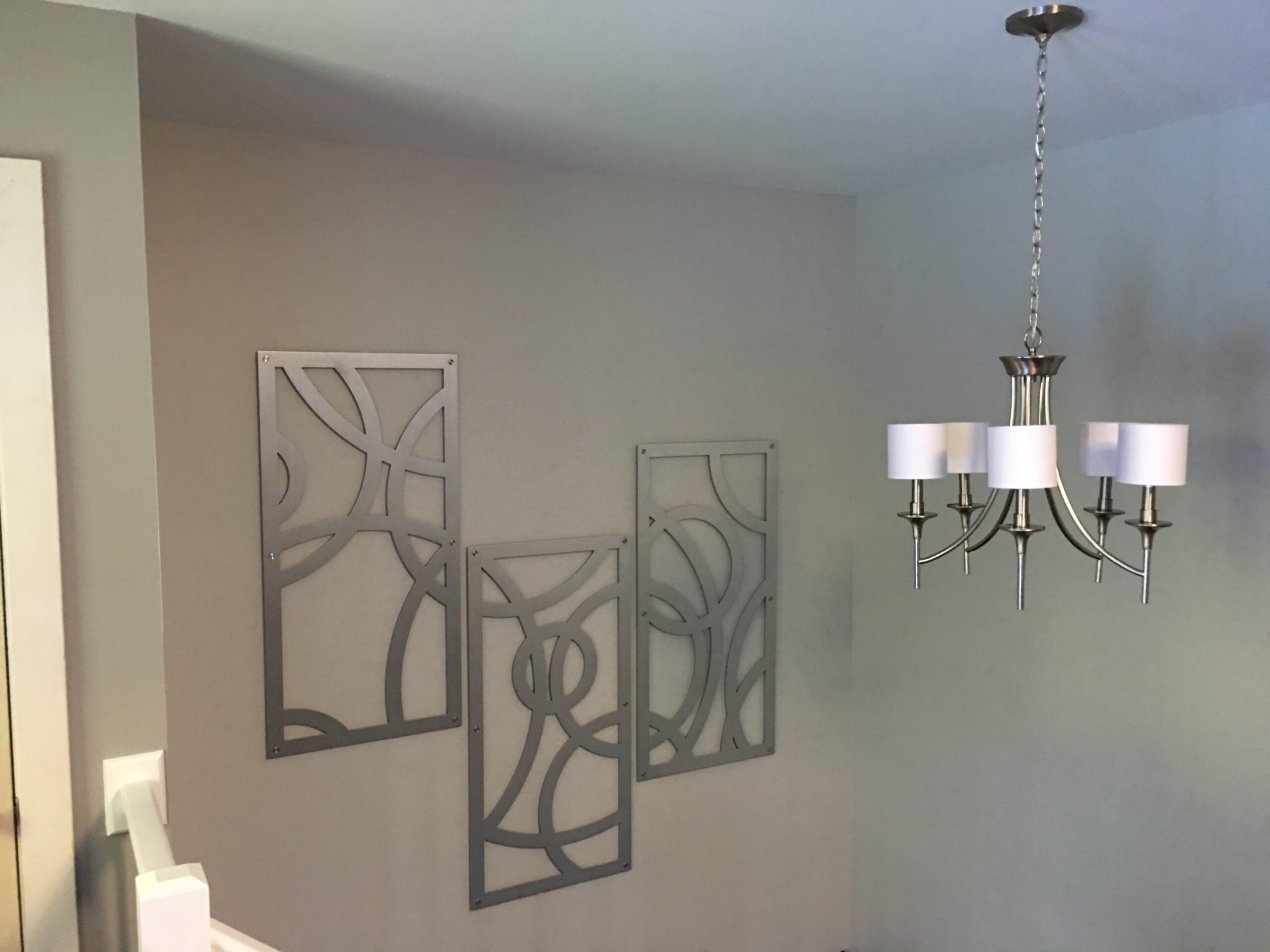 Three decorative metal wall panels and a modern chandelier hang in a well-lit room.