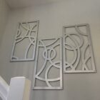 Three decorative metal panels with abstract designs hang on a light-colored wall near a staircase.