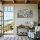 A coastal living room features metal coral art, a wooden table with decor, and a view of the ocean.