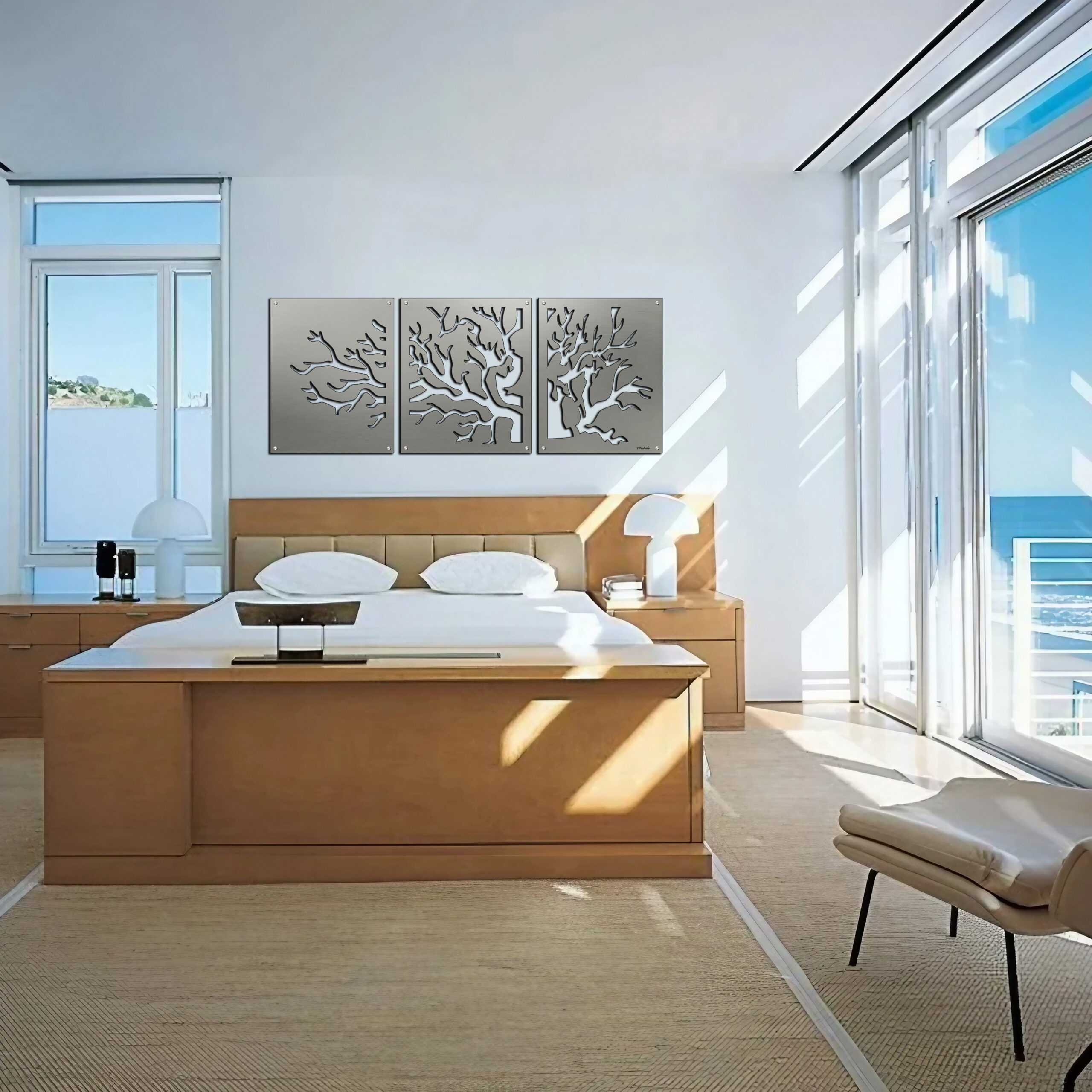 Bright bedroom with a large bed, three tree-themed wall art pieces, and ocean view through glass doors.