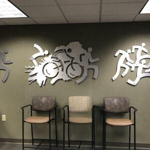 Three metal wall sculptures depict running figures and a cyclist, with empty chairs in the foreground.
