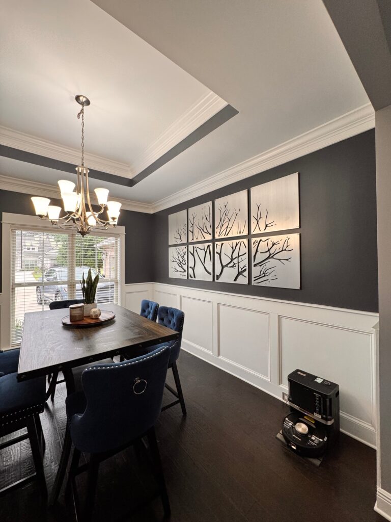 Dining room features a wooden table, blue chairs, and tree artwork on dark walls. A vacuum sits on the floor.