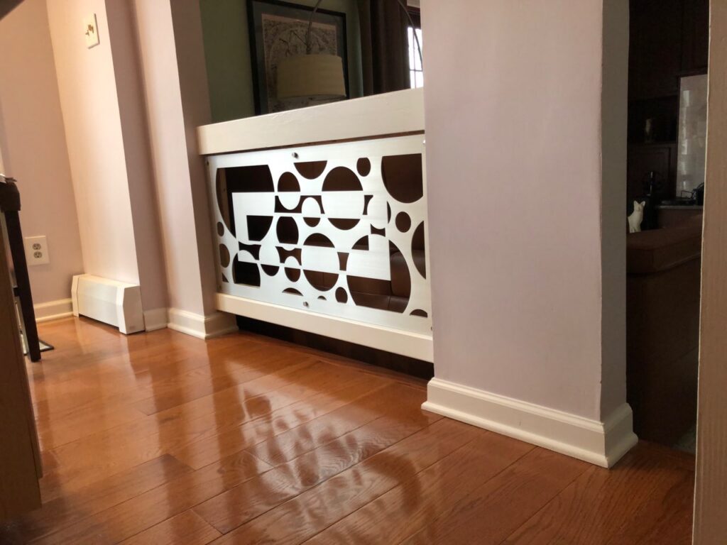 Wooden railing with circular cutouts separates two rooms, hardwood floor visible. Light from nearby window.