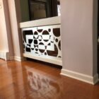 Wooden railing with circular cutouts separates two rooms, hardwood floor visible. Light from nearby window.