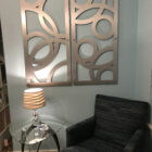 Two decorative metal panels hang on a light blue wall above a glass side table with a lamp and a striped armchair.