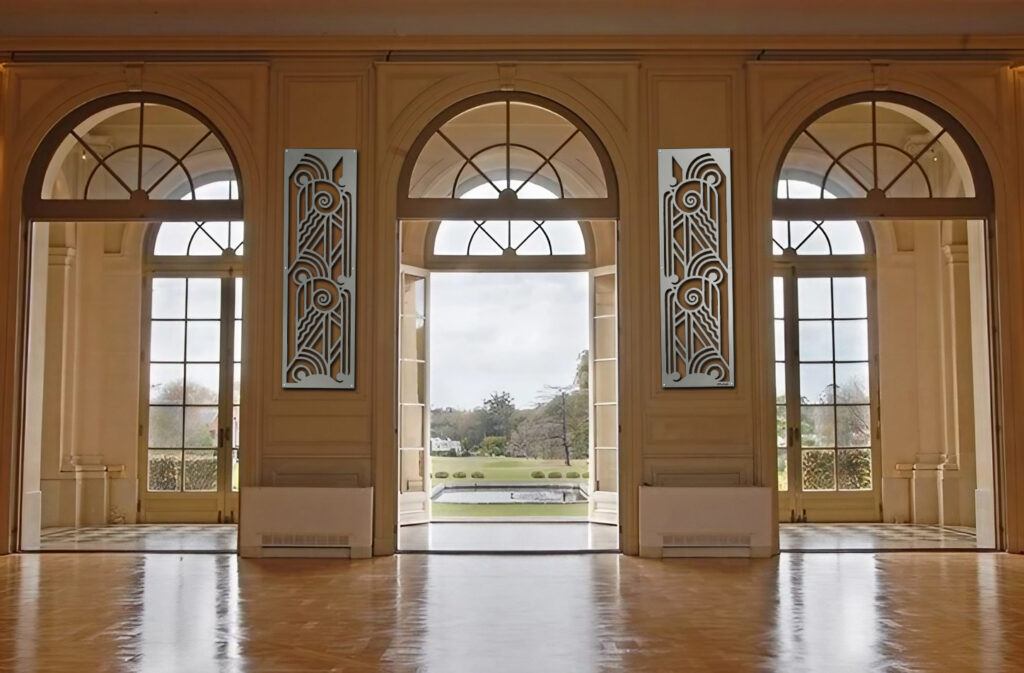 Elegant ballroom with large arched windows and decorative wall panels, revealing a garden view outside.