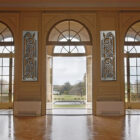 Elegant ballroom with large arched windows and decorative wall panels, revealing a garden view outside.
