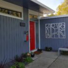 Modern house exterior with gray siding, red door, decorative wall art, and potted plants. Address number 3760 visible.