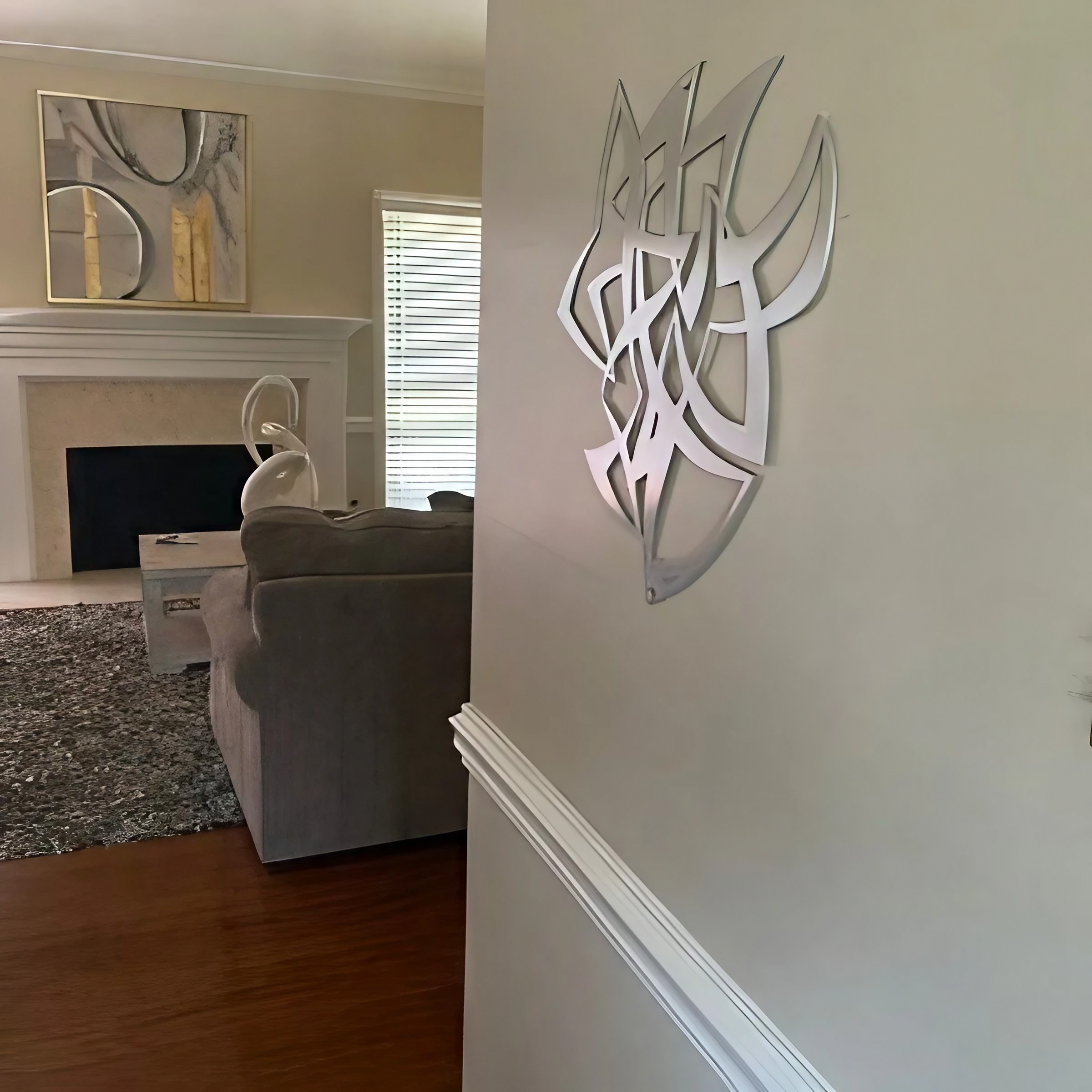 Modern wall art hangs beside a doorway, with a gray sofa and fireplace visible in the living room.
