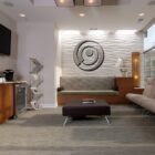 Modern office waiting area with a sofa, coffee station, decorative lighting, and a wall art piece.