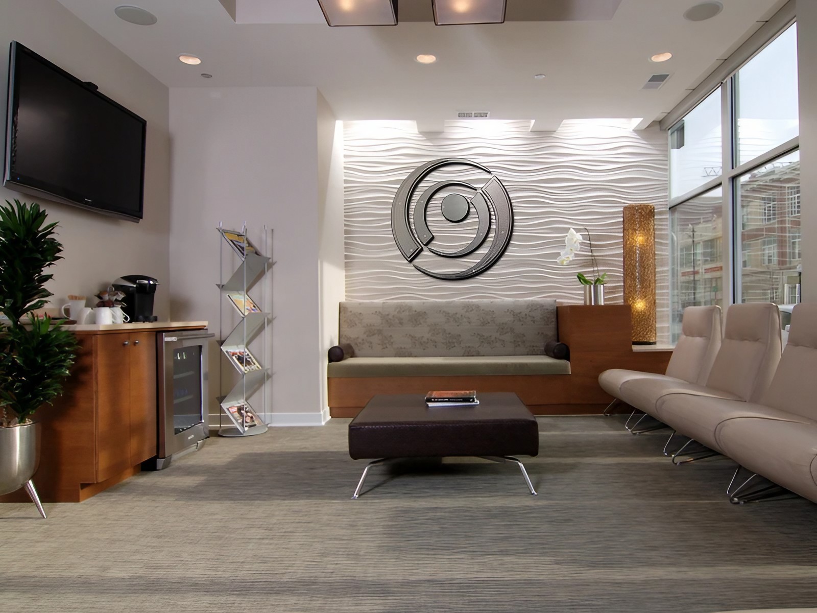 Modern office waiting area with a sofa, coffee station, decorative lighting, and a wall art piece.