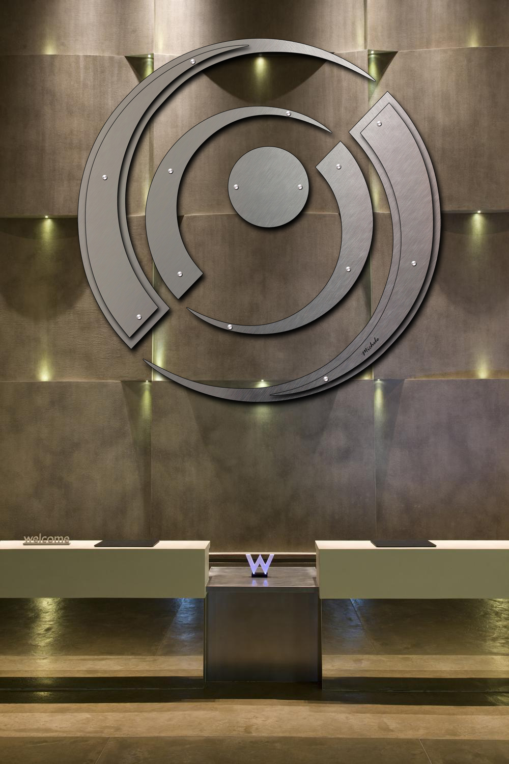 Modern reception area features a large circular metal art piece and a sleek front desk with a "W" logo.
