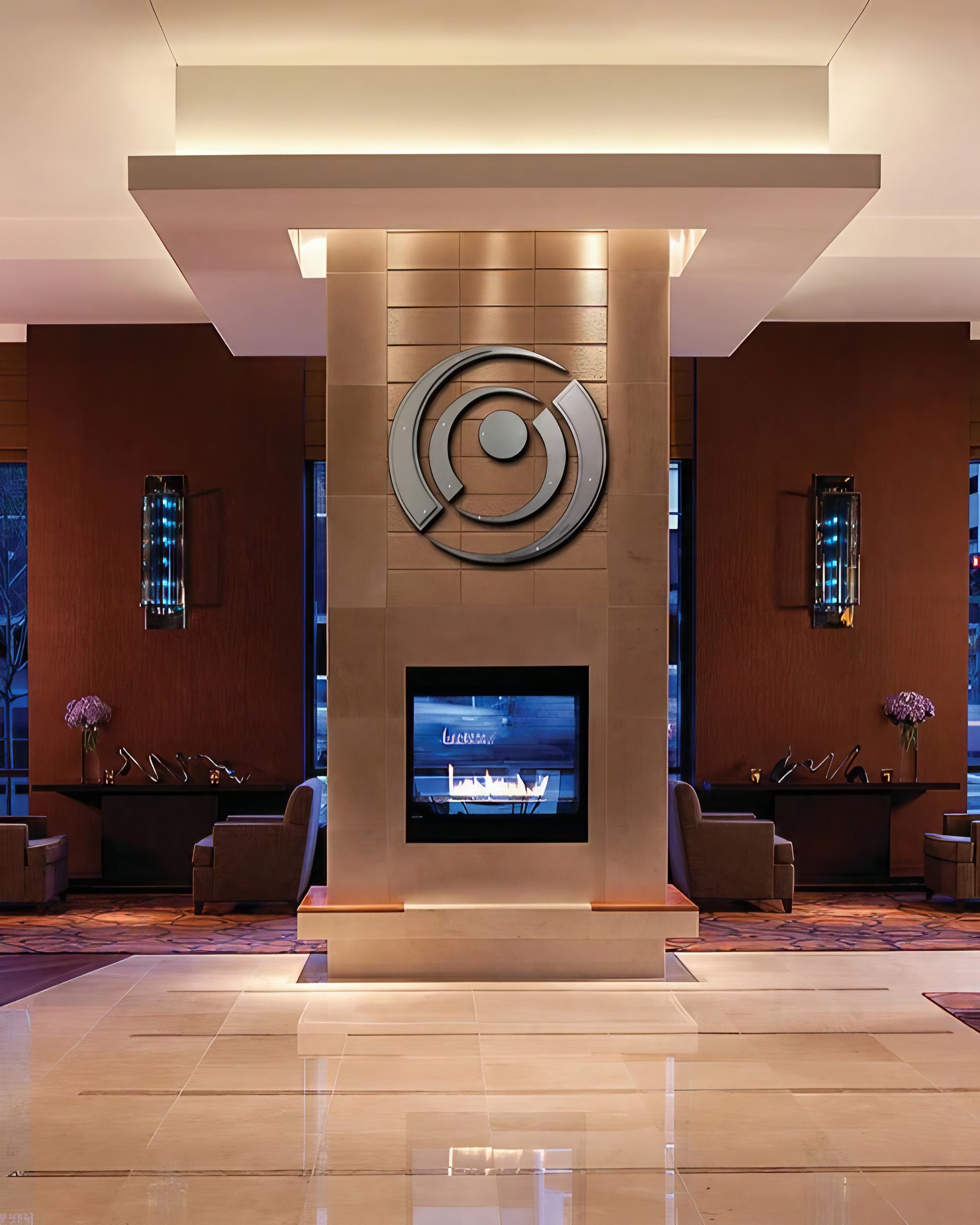 Modern lobby with a central fireplace, decorative wall art, and comfortable seating areas.