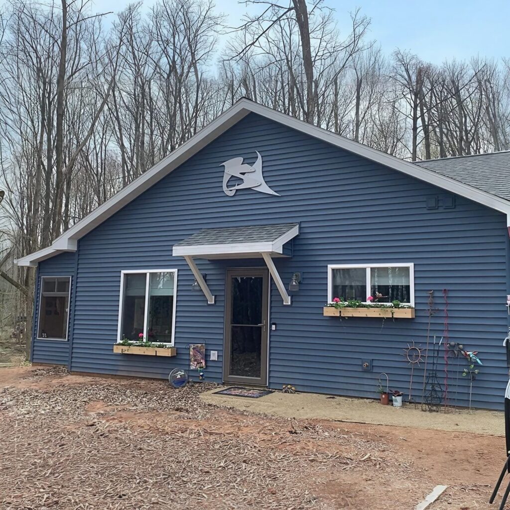 Blue house with a decorative emblem, surrounded by trees, features flower boxes under windows.