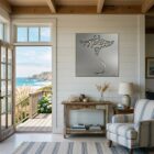 A coastal living room features a manta ray metal art piece on the wall, with ocean views through the doorway.