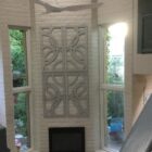 Bright living space features a large decorative wall panel, windows, and a fireplace. A ceiling fan hangs above.