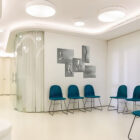 A modern office waiting area with teal chairs and anatomical art on the wall.
