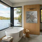 A modern bathroom features a sea turtle metal art piece on a wooden wall, overlooking a scenic lake view.
