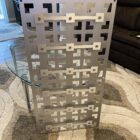 A decorative metal panel with geometric cutouts stands in a living room near a glass table and brown couch.