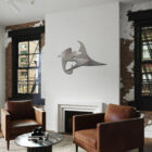 Modern living room featuring two brown chairs, a round table, and a metal wall sculpture.